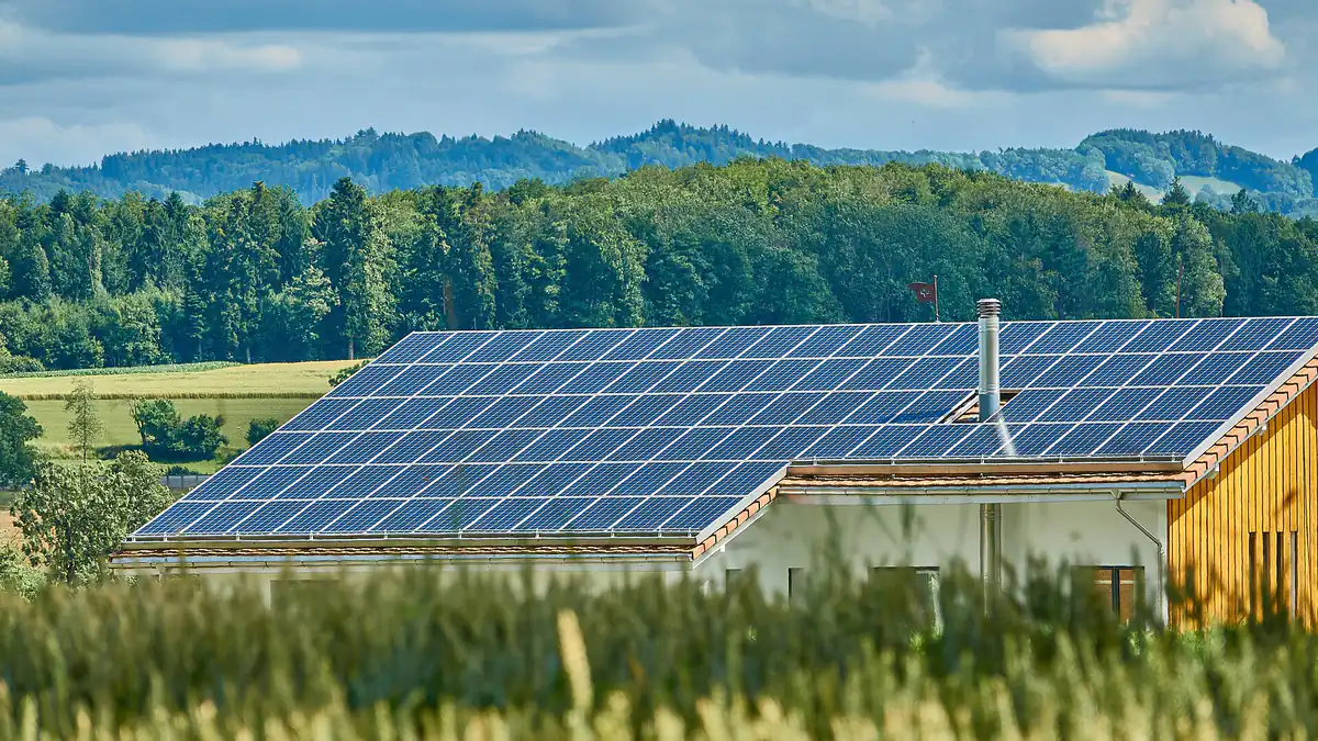 Une maison individuelle à la campagne, dont tout le versant de toit est couvert de panneaux photovoltaïques, devant une forêt.